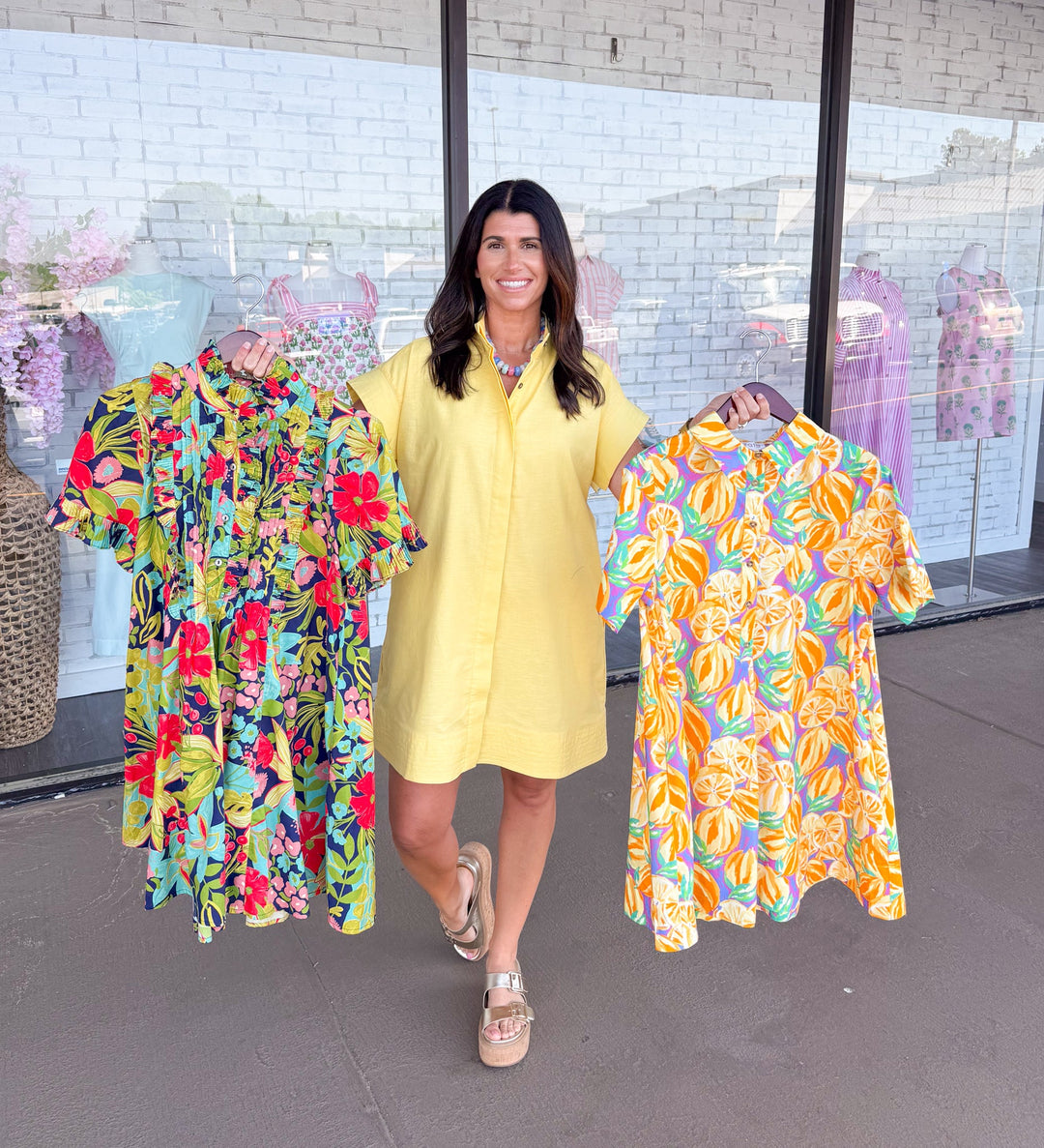 Woman wearing yellow linen dress holding two summer printed dresses